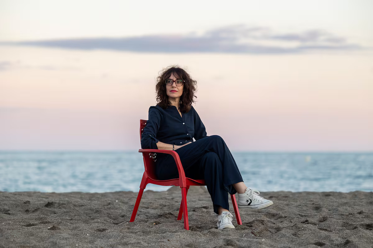 Una chica sentada en una silla roja en la playa contaminando la vista